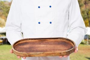 chef-kok houdt een leeg houten dienblad op de straatachtergrond vast foto