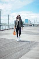 spelen ukulele van jong mooi Aziatisch vrouw vervelend jasje en zwart jeans poseren buitenshuis foto