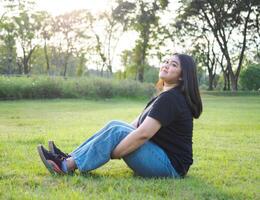 portret jong vrouw meisje Aziatisch mollig schattig mooi lang zwart haar- een persoon slijtage zwart overhemd zittend met armen verheven vrij in tuin park buitenshuis avond zonlicht vers gelukkig kom tot rust consument dag foto