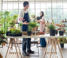 portret tuinman jong Aziatisch Mens vrouw twee persoon staand glimlachen op zoek hand- Holding helpen versieren boom blad groen in kalmte werk in kamer winkel huis fabriek wit muur. hobby baan gelukkig en zorg concept foto