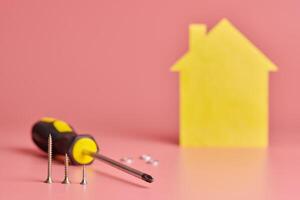 huisreparatie en opnieuw ingericht concept. renovatie huis. schroeven en gele huis vormige figuur op roze achtergrond. foto