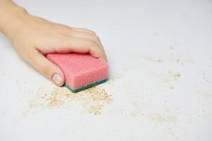 keukentafel schoonmaken. roze spons in de hand van de vrouw verwijdert vuil, broodkruimels en restjes. huishoudelijke taken foto