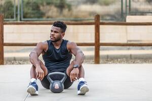 gespierd Afrikaanse Amerikaans sportman resting met kettlebell buitenshuis foto