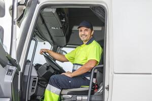 glimlachen mannetje bestuurder zittend in vrachtauto en op zoek Bij camera foto