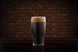 geïsoleerd bezweet glas verfrissend donker bier van de tap met bakstenen muur achtergrond.