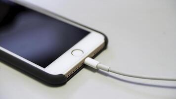 dichtbij omhoog van de appel iphone met de opladen kabel aan het liegen Aan de wit tafel. media. werkwijze van opladen van een modern apparaat verbonden naar USB kabel. foto