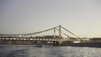 mooi stad landschap met rivier- gloeiend brug en drijvend boot. actie. boot drijft Aan rivier- Aan achtergrond van gloeiend brug Bij zonsondergang foto