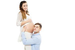 jonge aantrekkelijke paar zwangere moeder en gelukkige vader die zwangere buik luistert foto