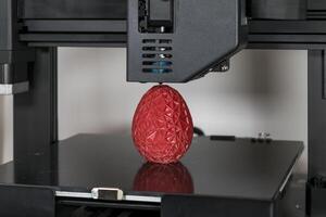 dichtbij omhoog van een 3d printer het drukken een rood veelhoekige ei foto