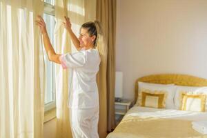 beeld van mooi hotel hulp in de huishouding opening venster gordijnen in een kamer. foto