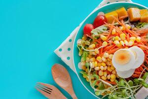 vers salade groente met gekookt kip ei, houten lepel en vork Aan blauw achtergrond foto