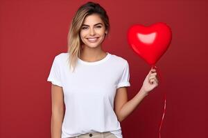 ai gegenereerd jong blond vrouw met hart ballon in de hand, vervelend bella canvas wit overhemd model, rood achtergrond. valentijnsdag dag of verjaardag ontwerp t-shirt sjabloon, afdrukken presentatie maquette. foto