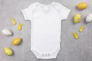 wit baby meisje of jongen bodysuit mockup vlak leggen met Pasen eieren en konijntjes decoratie Aan de grijs beton achtergrond. ontwerp Onesie sjabloon, afdrukken presentatie bespotten omhoog. top visie. foto