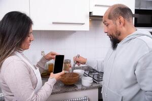 vrouw records met mobiel telefoon terwijl haar partner bereidt zich voor koekje deeg. foto