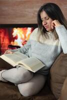 vrouw geniet lezing een boek van haar sofa Bij huis. foto
