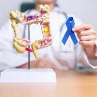 dokter Holding blauw lint met menselijk dikke darm anatomie model. maart colorectaal kanker bewustzijn maand, colon ziekte, groot darm, ulceratief colitis, spijsvertering systeem en Gezondheid concept foto