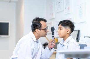 optometrist aan het doen zicht testen voor kind geduldig in kliniek, Indisch kind kiezen bril in optiek op te slaan, jongen aan het doen oog test controle examen met optometrist in optisch winkel foto