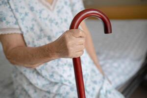 Aziatisch ouderen onbekwaamheid vrouw Holding wandelen stok, hout riet, ronde handvat, wandelen steun voor helpen naar wandelen. foto