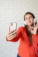 jonge kaukasische vrouw die oortelefoons draagt die op mobiel babbelen die goed teken tonen foto