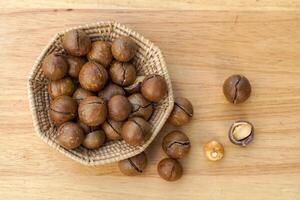 top visie van mand van geroosterd macadamia zaden Aan een houten tafel met macadamia noten verspreiding uit. de zaden hebben smaak en een geurig structuur rijk in veel voedingsstoffen. foto