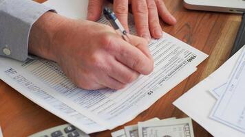 Mens zittend Bij tafel met document en pen, dichtbij omhoog hand- vulling belasting het formulier foto