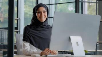 zelfverzekerd geslaagd elegant Arabisch zakenvrouw typen Aan computer aantrekkelijk moslim vrouw in hijab professioneel arbeider ervaren manager ondernemer werken in modern kantoor poseren in werkplaats foto