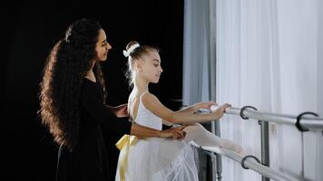 tiener meisje kind tiener ballerina in tutu luisteren advies van vrouw danser trainer leraar leren naar dans in dansen school- ballet barre uitrekken heup. vrouw trainer helpt correct positie foto