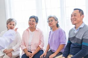 senior vrouwtjes en mannetje zittend Aan bank. ouder mensen zijn luisteren en genieten vergadering focus groep Bij leven kamer. blij zorgeloos gepensioneerd senior vrienden genieten van ontspanning Bij bijna huis. foto