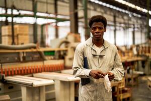 Afrikaanse Mens arbeiders bouwkunde staand met vertrouwen met werken suite jurk en hand- handschoen in voorkant machine. concept van slim industrie arbeider werkend. hout fabriek produceren hout gehemelte. foto