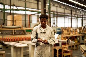 Afrikaanse Mens arbeiders bouwkunde staand met vertrouwen met werken suite jurk en hand- handschoen in voorkant machine. concept van slim industrie arbeider werkend. hout fabriek produceren hout gehemelte. foto