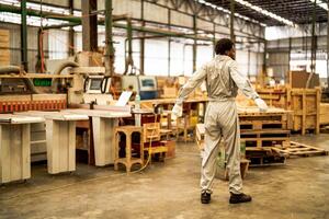 Afrikaanse Mens arbeiders bouwkunde staand met vertrouwen met werken suite jurk en hand- handschoen in voorkant machine. concept van slim industrie arbeider werkend. hout fabriek produceren hout gehemelte. foto