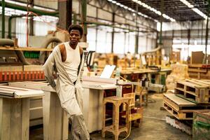 Afrikaanse Mens arbeiders bouwkunde staand met vertrouwen met werken suite jurk en hand- handschoen in voorkant machine. concept van slim industrie arbeider werkend. hout fabriek produceren hout gehemelte. foto