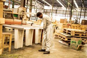 Afrikaanse Mens arbeiders bouwkunde staand met vertrouwen met werken suite jurk en hand- handschoen in voorkant machine. concept van slim industrie arbeider werkend. hout fabriek produceren hout gehemelte. foto