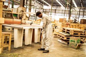 Afrikaanse Mens arbeiders bouwkunde staand met vertrouwen met werken suite jurk en hand- handschoen in voorkant machine. concept van slim industrie arbeider werkend. hout fabriek produceren hout gehemelte. foto