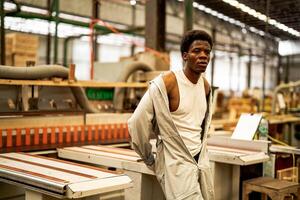 Afrikaanse Mens arbeiders bouwkunde staand met vertrouwen met werken suite jurk en hand- handschoen in voorkant machine. concept van slim industrie arbeider werkend. hout fabriek produceren hout gehemelte. foto