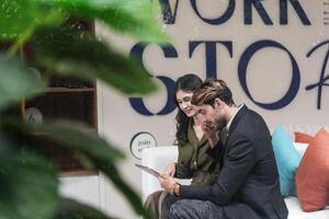 bedrijf mensen pratend Bij werkplaats kantoor. mannetje en vrouw collega's genieten ontspannende en zittend Aan bank. collega's bespreken over de project in de kantoor. team van jong mensen in kantoor. foto