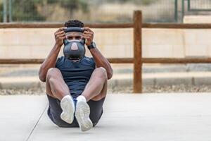 zwart Mens in activewear aan het doen buikspieren training met kettlebell gedurende buitenshuis oefening foto