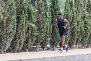 Afrikaanse Amerikaans Mens in activewear jogging langs park Aan zonnig dag foto