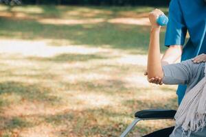 jong verpleegster of fysiotherapeut in scrubs helpen een gelukkig gepensioneerd oud vrouw Doen geschiktheid opdrachten met licht gewicht halters Bij huis. concept van fysiotherapie voor senioren foto