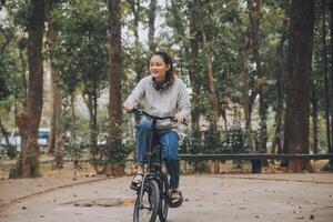 gelukkig Aziatisch jong vrouw wandelen en rijden fiets in park, straat stad haar glimlachen gebruik makend van fiets van vervoer, eco vriendelijk, mensen levensstijl concept. foto