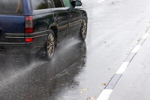 regen water spatten stromen van wielen van oud blauw auto dat in beweging snel Aan asfalt weg foto