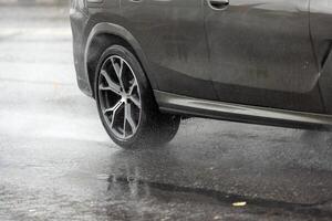 regen water spatten stromen van wielen van grijs auto dat in beweging snel Aan asfalt weg foto