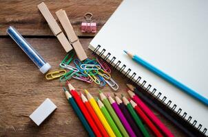 kleurpotloden, gummen, notitieboekje, klem Aan een houten vloer. foto