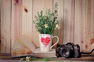 de bloemen geplaatst in een glas hout Aan de boeken en een camera in de achtergrond. foto