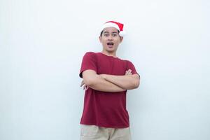 jong Aziatisch Mens vervelend een de kerstman claus hoed kruispunt zijn armen terwijl lachend, schok en lachend met een wit achtergrond voor zichtbaar communicatie foto