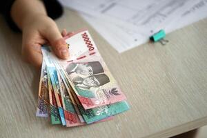 vrouw accountant hand- geven bundel van veel Indonesisch roepia geld rekeningen van nieuw serie foto