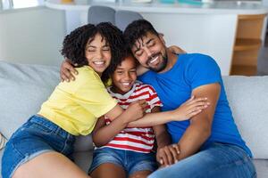 familie afbeelding van glimlachen jong mam en vader zitten Aan bankstel poseren met schattig weinig dochter, klein opgewonden grappig meisje knuffel gelukkig ouders, kom tot rust Aan sofa samen foto