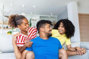 portret aantrekkelijk multi-etnisch vrouw man en kind binnenshuis. dichtbij omhoog getrouwd paar met weinig mooi dochter zittend samen glimlachen op zoek Bij camera. concept vriendelijk welzijn gelukkig familie foto