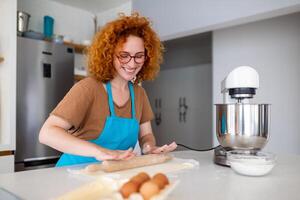 gelukkig aantrekkelijk jong volwassen vrouw huisvrouw bakker slijtage schort Holding pin rollend deeg Aan keuken tafel bakken gebakje concept Koken taart biscuit aan het doen bakkerij maken eigengemaakt pizza Bij huis foto