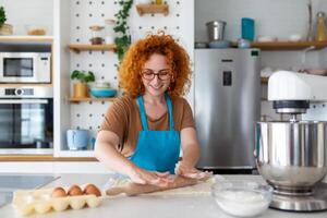 bakken concept. portret van blij vrouw kneden deeg in keuken interieur, vrolijk vrouw in schort hebben pret terwijl voorbereidingen treffen eigengemaakt gebakje, foto